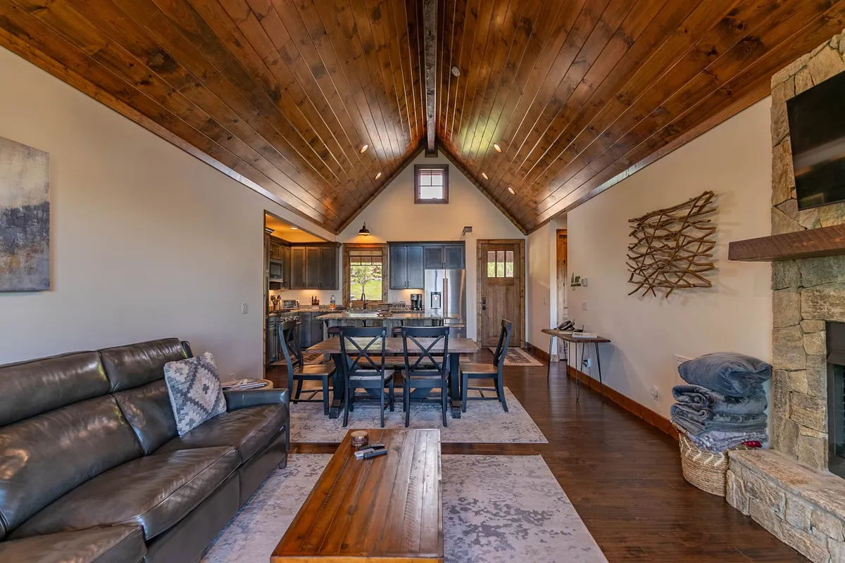 This image features a welcoming open-concept interior with a leather sofa, a dining table set for a meal, a view into the kitchen area, and a glowing fireplace. The design invites gatherings and showcases the central living space where relaxation, dining, and cooking all flow together.