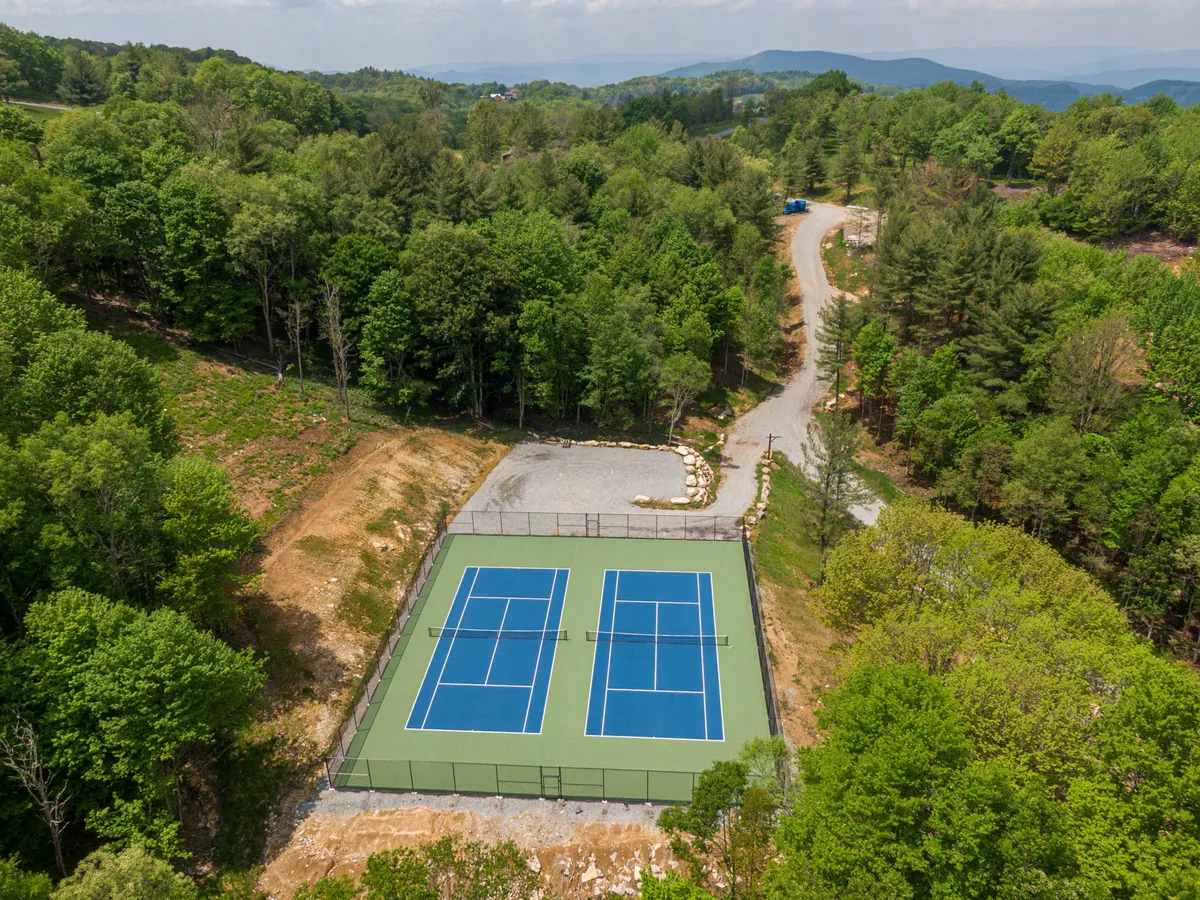 Tennis courts bordered by trees and a gravel road, offering a space for friendly matches, active recreation, and social gatherings in a natural setting.