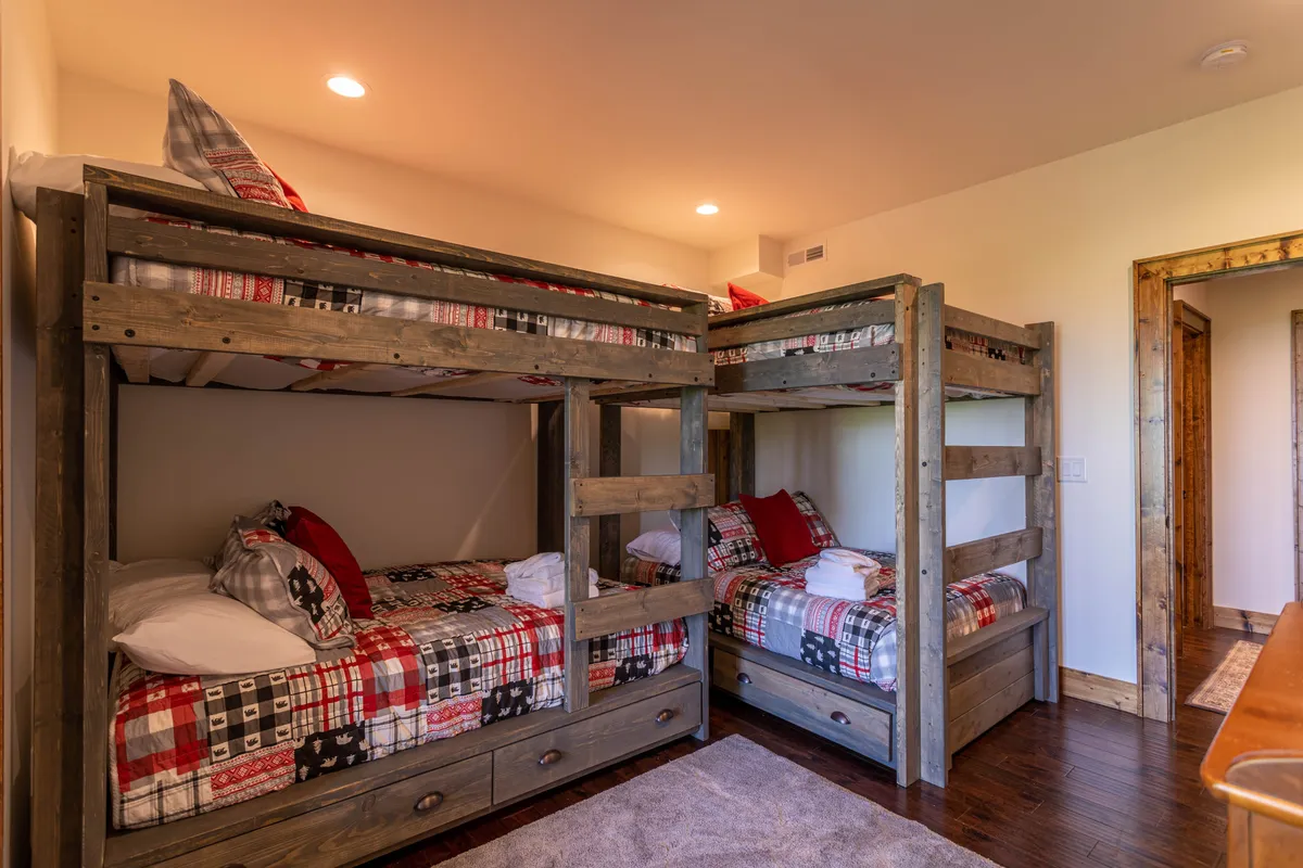 A warm, inviting bunk room with sturdy wooden bunk beds dressed in plaid bedding and complemented by matching wooden furniture. The setup radiates a sense of fun and togetherness, making it ideal for kids, teens, or groups seeking a sleepover environment.