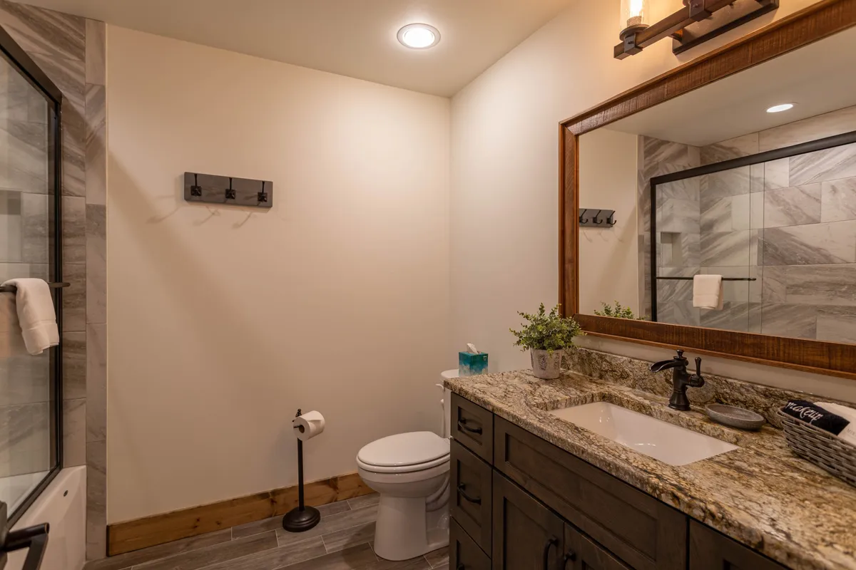 A well-appointed bathroom with a granite countertop, large mirror, shower area, and decorative plant, exuding a clean and serene ambiance. The design ensures comfort and privacy for lower-level guests.