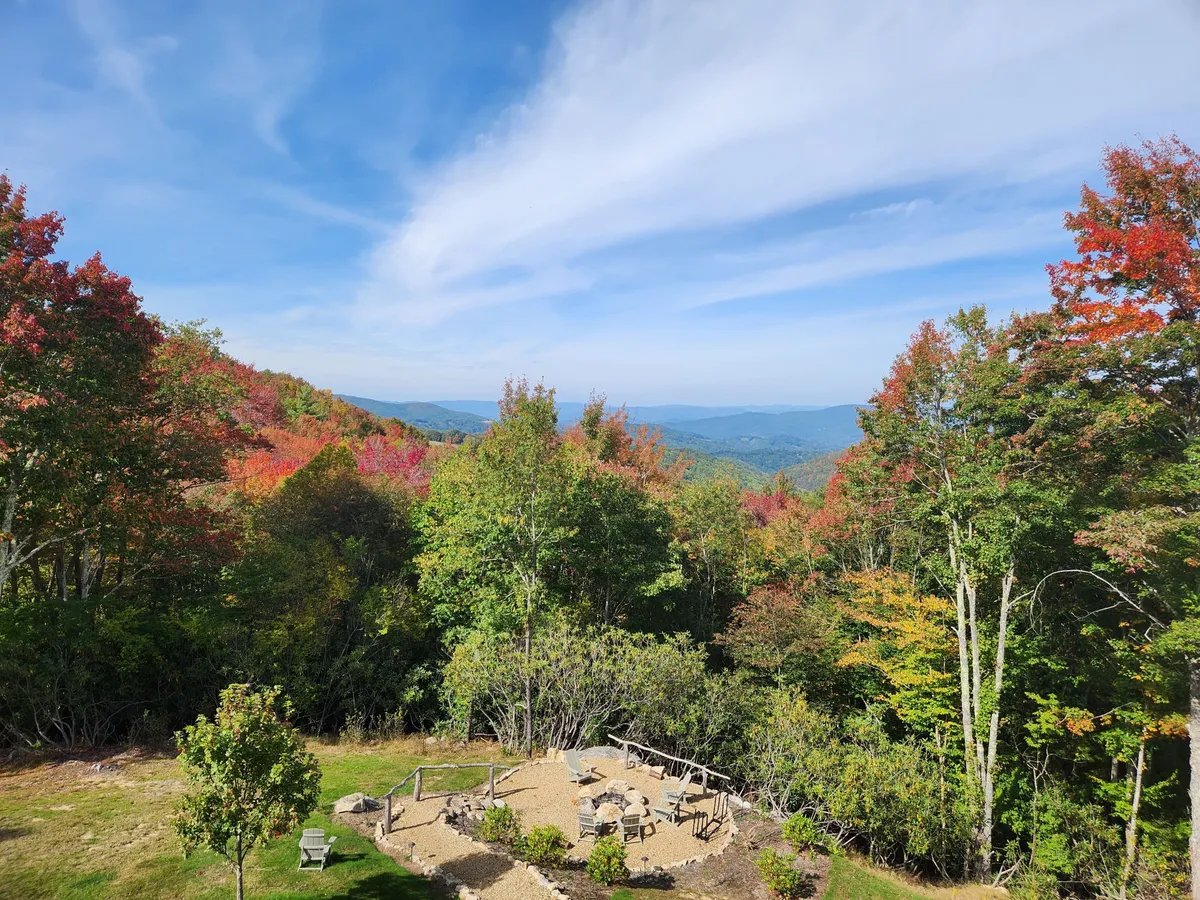 This image features a vibrant patio area with seating, set against a backdrop of colorful mountain foliage and a distant mountainous horizon. The scene is bathed in sunset light, creating a serene setting perfect for relaxing after a day of adventure. The patio is clearly oriented toward views and outdoor enjoyment, with plenty of open sky for stargazing.