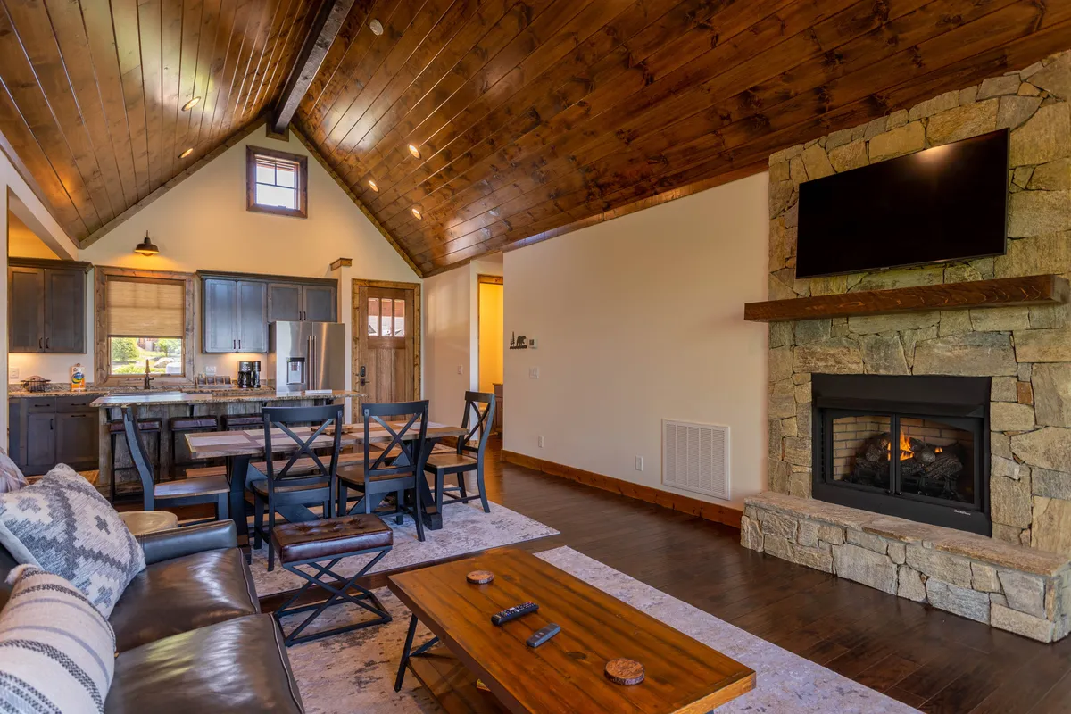 An inviting perspective that showcases a stone fireplace anchoring the living area, with a comfortable sofa and a dining table nearby. The space feels intimate and designed for relaxation, meals, and movie nights.