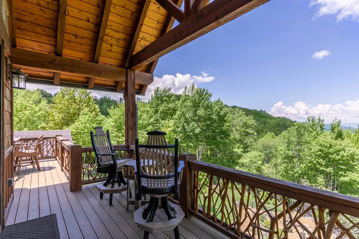 A wooden deck furnished with classic rocking chairs and surrounded by lush greenery with distant mountain views. The setup invites relaxation, conversation, and taking in the outdoors, with plenty of space for social gatherings or quiet reflection.