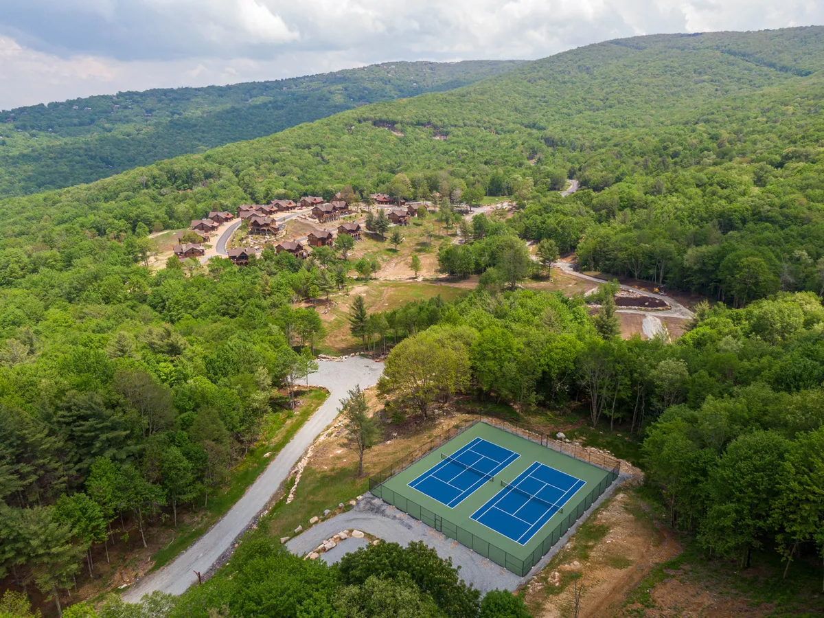 A view of community tennis courts set against a backdrop of mountains and greenery, with residential units nearby. The vibrant scene suggests activities, events, and a lively communal atmosphere.