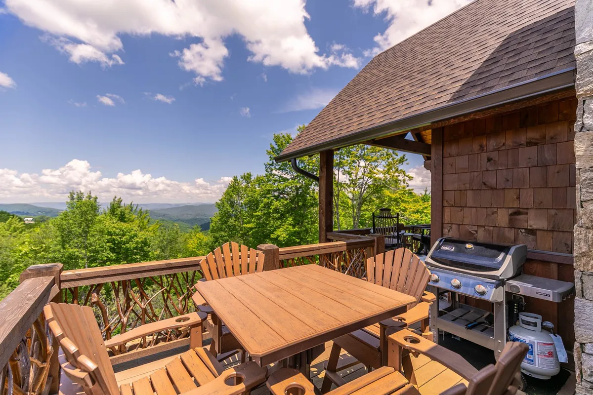 A serene deck scene with wooden patio furniture and a grill set against a mountain view. The arrangement suggests al fresco meals, relaxed conversations, and shared experiences, all within a stunning natural setting.