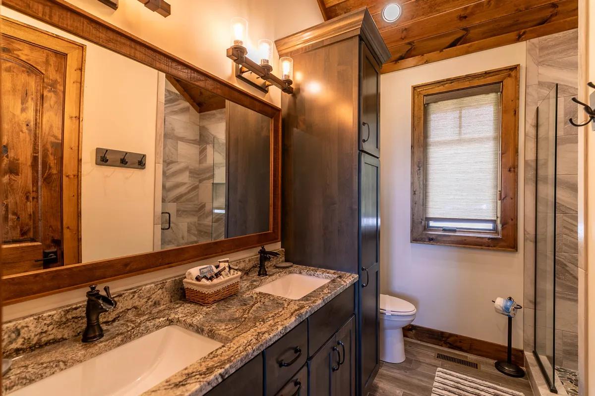 A modern bathroom with a double vanity sink, large mirror, stylish granite countertops, a separate shower area, and warm wood accents. The space feels both calming and upscale.